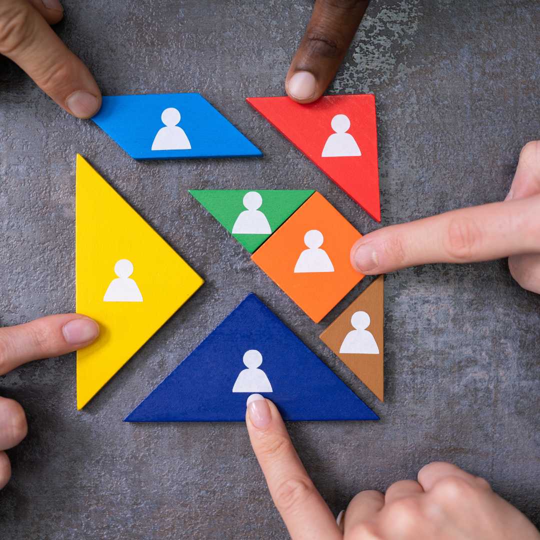 Opstellingen- handen, Kr8stroom Handen plaatsen kleurrijke vormen met pictogrammen van personen op een tafel.