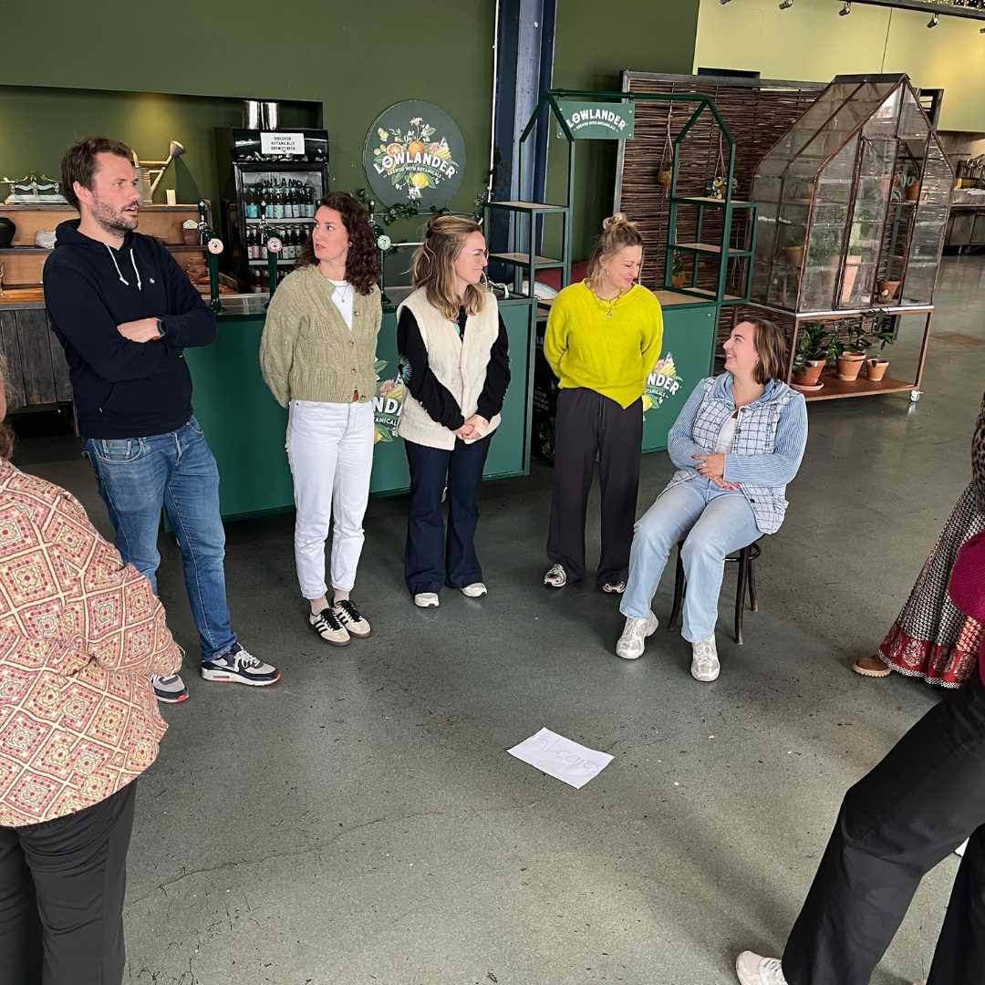 opstelling - vrouw zit, Kr8stroom Groep deelnemers tijdens een opstelling; één vrouw zit op een stoel, anderen staan in een halve cirkel.