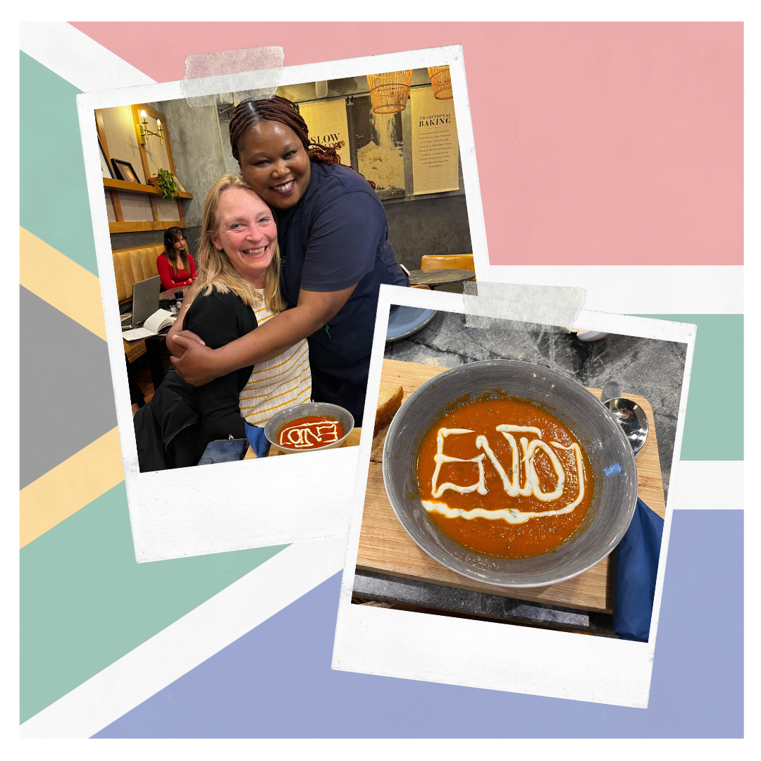 kr8stroom.nl – enjoy Vrouw in een lunchroom in Zuid-Afrika met serveerster en een kom tomatensoep waarop met room het woord “END” of “ENJOY” te lezen is.