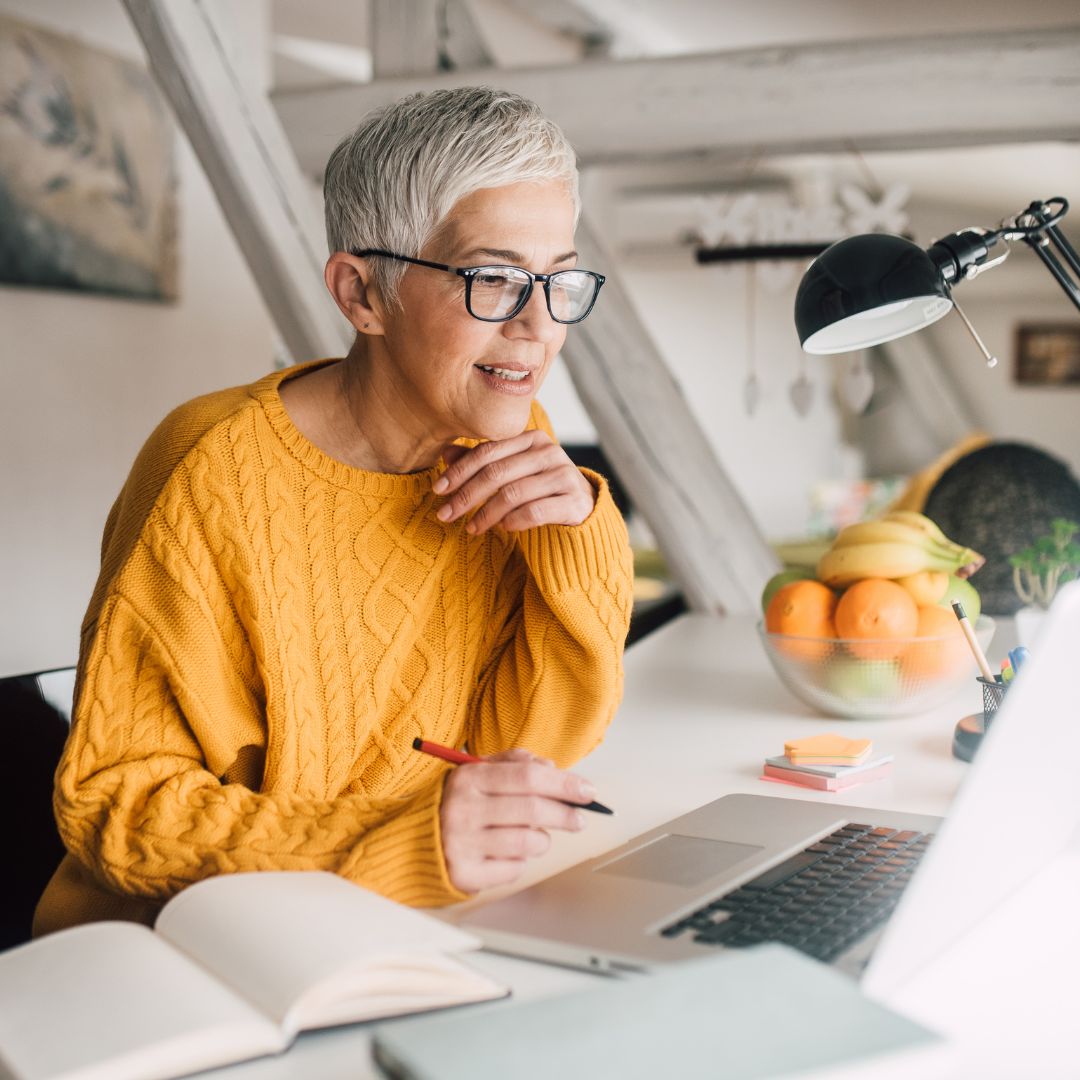 Vrouw met korte grijze haren werkt achter een laptop, als beeld bij helder kiezen, werken en grenzen bewaken.