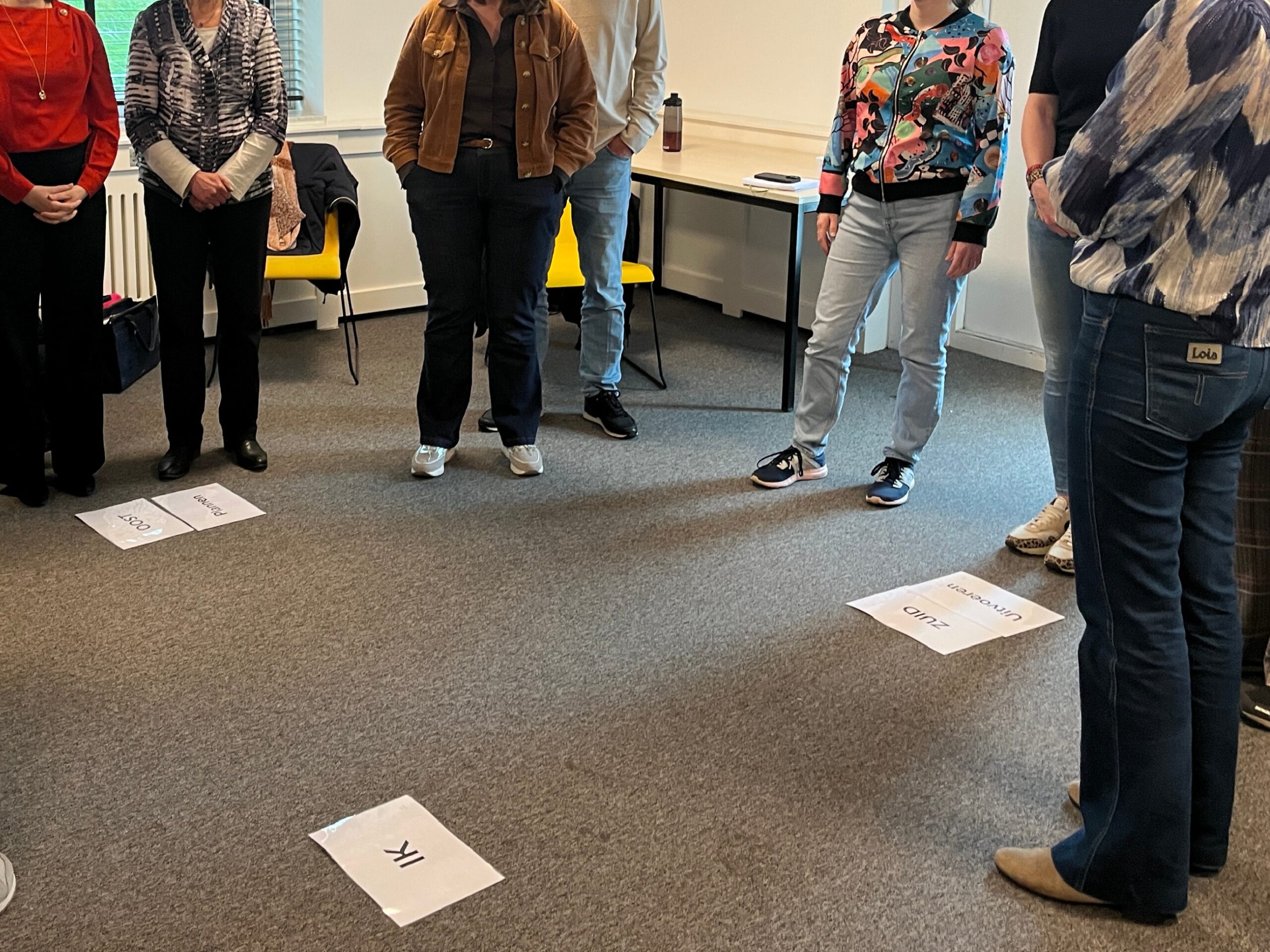 Deelnemers staan in een kring tijdens een systemische opstelling, met vloerankers die verschillende personen en posities vertegenwoordigen.